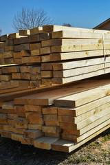 Stacked lumber on blue sky.Folded wood.Closeup wooden boards.The surface of the end of the board.Lots of planks stacked on top of each other in the warehouse.Lumber for use in construction.