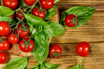 Fresh cherry tomatoes with green basil leaves on a wooden table. Top view