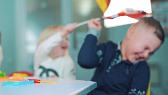 Little boy and a girl with flags at class. German and British flags in the hands of small children sitting at the table. Kids wave flags indoors.