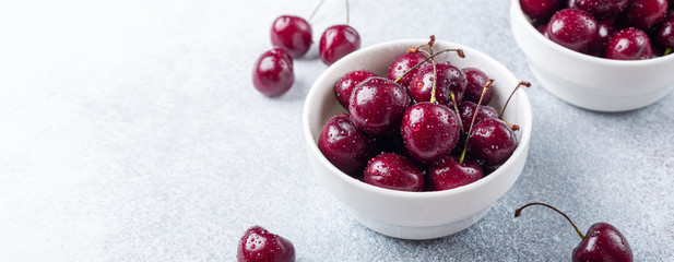 Fresh ripe red cherries in a white bowl on a gray stone background Closeup Water drops Horizontal banner