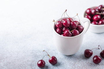 Fresh ripe red cherries in a white mug on a gray stone background Closeup Water drops Top view