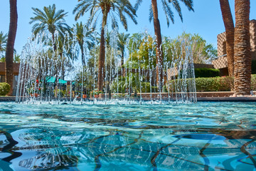 Fototapeta na wymiar Pool with ripples caused by fountain jets with palm trees in background