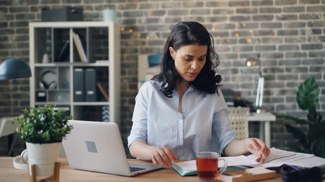 Worried manager pretty lady is using laptop and reading paper document working in office alone with sad face. Problems at work and modern business concept.
