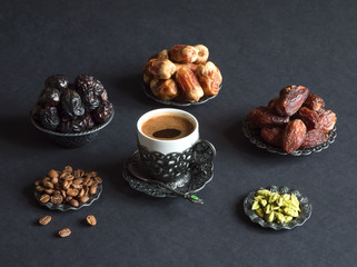 Dates and cup of Arabic coffee with cardamom on the black table.