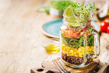 Fresh spring salad with salmon, quinoa, arugula, cress salad and corn in a mason jar for a snack with you. The concept of healthy proper nutrition.