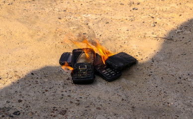 Obraz na płótnie Canvas burnt mobile phones on textural concrete background. Concept: Danger of using low-quality cell phones.