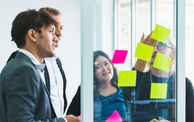 Group of business colleague people meeting discussing idea of work in sticky notes on glass wall at office