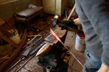 Blacksmith forging red-hot metal with hammer.