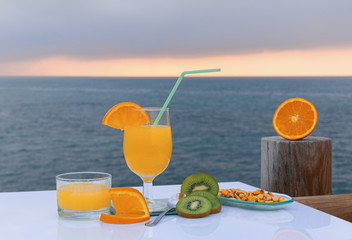 Colorful fruit snack with the sea in the background - Orange juice, kiwi slices, sweet corn and ripe orange slices on a white table