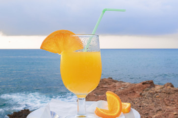 Close-up of a tasty orange juice with slices of ripe orange - Rocks on the sea coast background