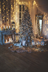 warm cozy evening in Christmas room interior design,Xmas tree decorated by lights gifts,toys, deer,candles, lanterns, garland lighting indoors fireplace.holiday.magic New year