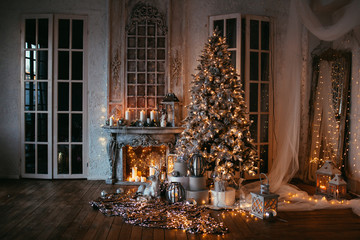 warm cozy evening in Christmas room interior design,Xmas tree decorated by lights gifts,toys, deer,candles, lanterns, garland lighting indoors fireplace.holiday.magic New year