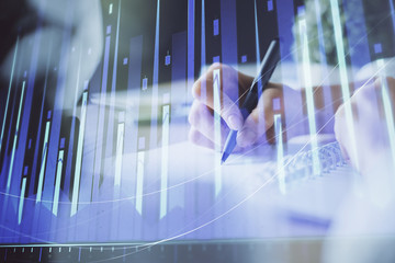 Financial forex graph displayed on hands taking notes background. Concept of research. Multi exposure