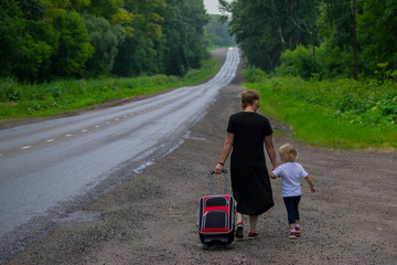 Mom and daughter go with a suitcase along the road.