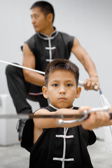 Father and son are engaged in Wushu in the city. The photo illustrates a healthy lifestyle and sport. The father trains the son. Close-up of son and father with swords.