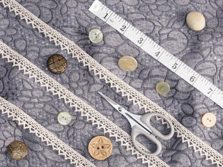 Lace, needle case, tape measure, buttons, scissors on a background of gray fabric. Concept sewing...