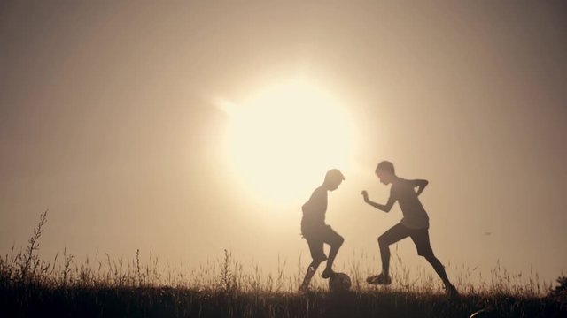 Two boys playing football at sunset. Silhouette of children playing with a ball at sunset. The concept of a happy family and a healthy lifestyle