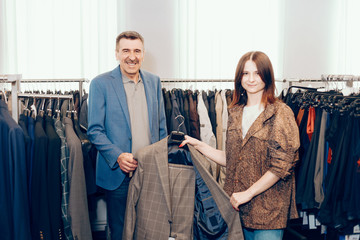 Obraz premium man select clothes in a boutique. female seller stylist helps to choose and try on clothes.
