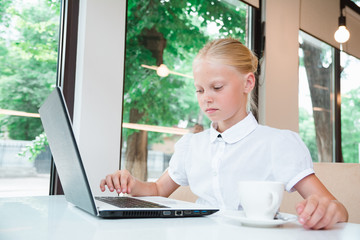 Portrait of child behind a laptop in cafe. Internet and telephone communications.