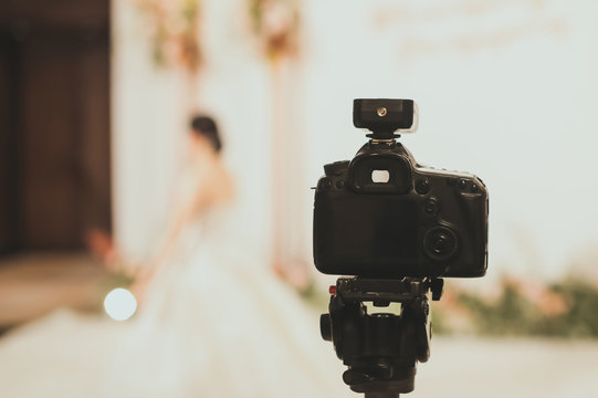 Close-up of professional DSLR digitak camera attached with tripod in wedding ceremony and with bride in wedding dress blurred out in background