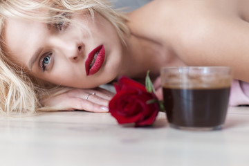 Obraz na płótnie Canvas beautiful blond girl lies on the floor with a cup of hot morning coffee and a bouquet of roses