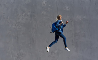 Fototapeta na wymiar Full body Portrait of happy young woman walking with bag and cellphone. Cheerful student jumping in air over gray background