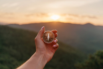 Female hand with compass in summer mountains at sunrise, pov. - obrazy, fototapety, plakaty