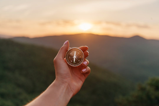 Female hand with compass in summer mountains at sunrise, pov.