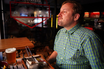 a man in a green shirt sitting at a bar table drinking beer and eating French fries with a disgruntled face