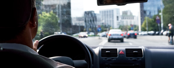 Man's hands of a driver on steering wheel in car on asphalt road in city