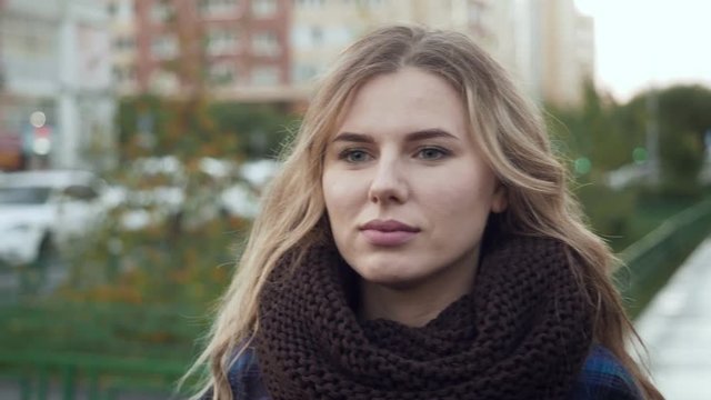 Gorgeous young blond woman in big knit scarf outdoors.