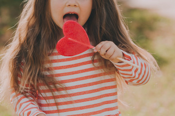 Cute baby girl with a red heart-shaped candy.