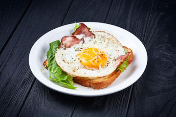 Close up view on toast with fried egg, bacon melted cheese and lettuce. Breakfast food. Fried toast on dark background. Snack. Copy space