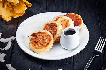 Cottage cheese pancakes served on white plate with hot chocolate on dark wooden background. Traditional homemade ukrainian food Syrniki. Gourmet Breakfast. Dessert cuisine