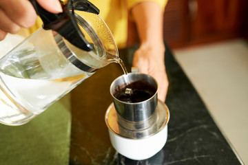 Close-up image of woman filling traditional Vietnamese coffee press with hot water