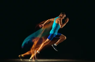 Fotobehang Professional male runner training isolated on black studio background in mixed light. Man in sportsuit practicing in run or jogging. Healthy lifestyle, sport, workout, motion and action concept. © master1305