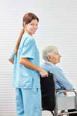 Obraz premium Young caregiver pushes senior woman in wheelchair