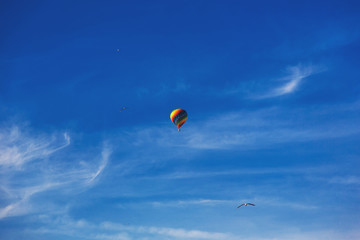 Balloon flying through the blue sky among the clouds. Freedom, adventure, loneliness. Birds are stolen around