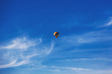 Fototapeta premium Balloon flying through the blue sky among the clouds. Freedom, adventure, loneliness.