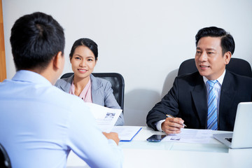 Young applicant talking to smiling human resources managers at office meeting