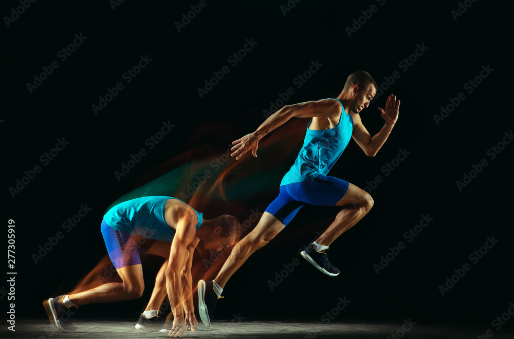 Wall mural Professional male runner training isolated on black studio background in mixed light. Man in sportsuit practicing in run or jogging. Healthy lifestyle, sport, workout, motion and action concept.