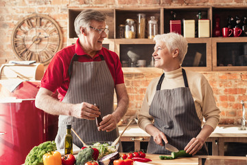 Cheerful senior man and woman cooking healthy salad at kitchen