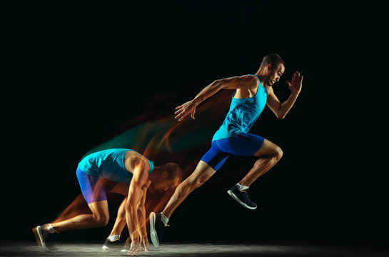 Professional Male Runner Training Isolated On Black Studio Background In Mixed Light. Man In Sportsuit Practicing In Run Or Jogging. Healthy Lifestyle, Sport, Workout, Motion And Action Concept.