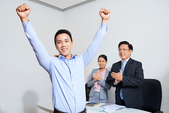 Excited happy young Asian businessman raising arms and celebrating promotion after meeting with comany CEO and human resources manager