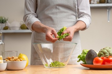 Chef adds green lettuce leaves, stir, in the process of a vegetarian salad in the home kitchen. Light background. restaurant menu, menu, recipe book. Healthy food, detox