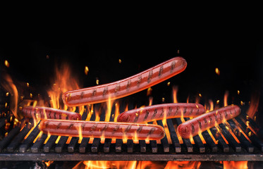 Sausages on the burning grill grate and tongues of fire flame.