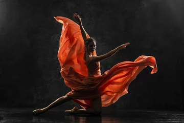 Rollo Ballerina. Silhouettenfoto einer jungen Balletttänzerin in einem langen pfirsichfarbenen Kleid, Spitzenschuhen mit Bändern. Das Mädchen führt eine anmutige Tanzbewegung durch. Schönes klassisches Ballett. Ballettstudios. © Sanklinarika