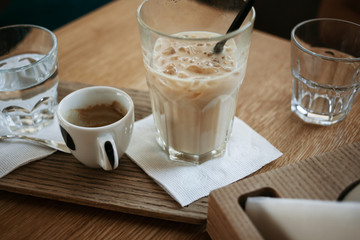 Coffee break in the working time. An empty cup of espresso with a glass of ice latte on the wooden table in a cafe.