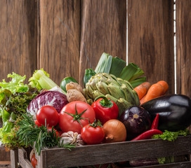 Fresh multi-colored vegetables in wooden crate. Wooden background.