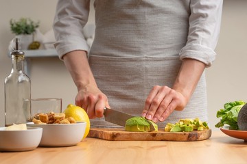 Cooking. Chef slices avocado, in the process of vegetarian salad in the home kitchen. Light background. Restaurant menu, menu, recipe book. Healthy nutrition, detox
